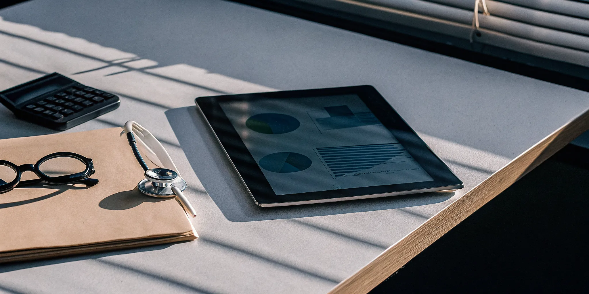 Comparing health care plans and prices on a tablet next to a calculator and stethoscope.